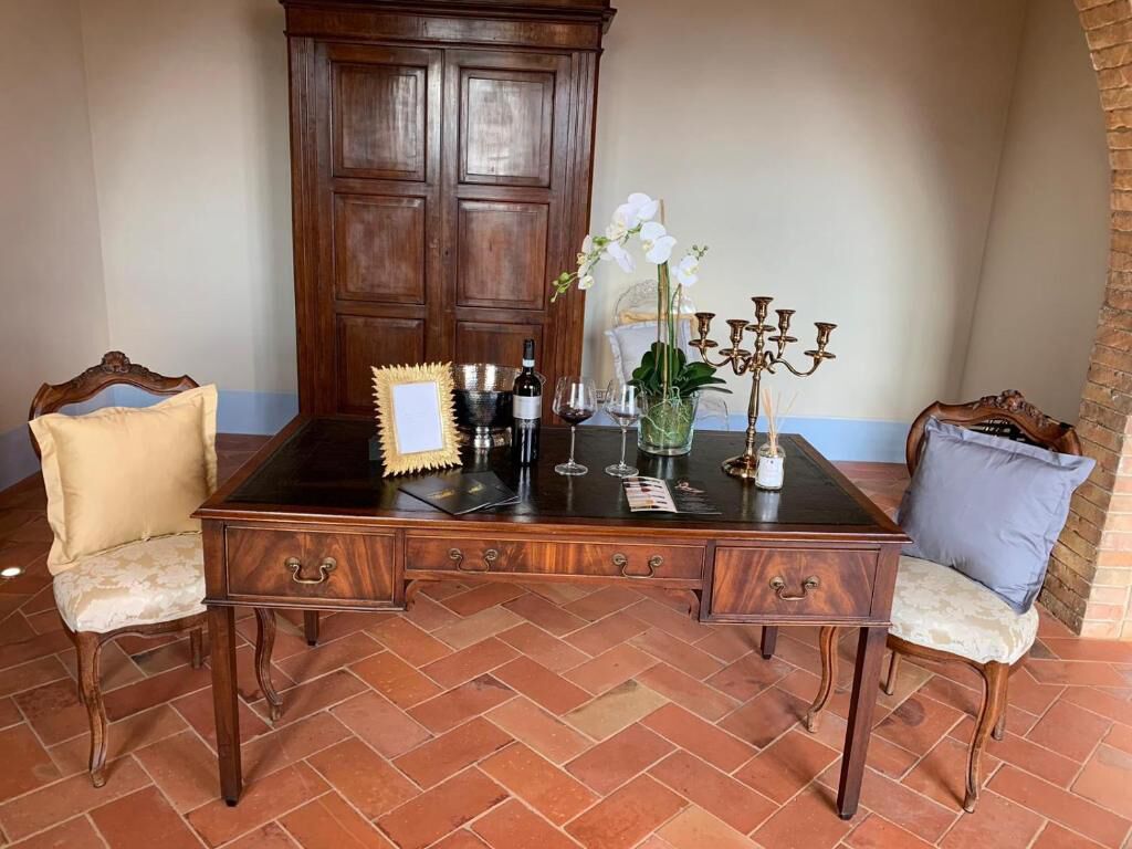 A wooden desk with two chairs, a vase with flowers, a wine bottle, and a candelabra.