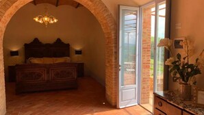 A bedroom with a brick archway, a wooden bed, a dresser, and a sliding glass door leading to a balcony. - Cordella in Valdorcia Truffle & Olive Oil Resort - Podere Borgasso (Montalcino)