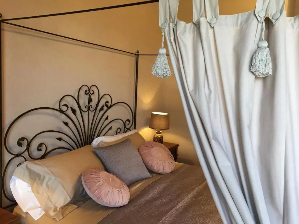 Una camera da letto con un letto a baldacchino, un comodino con una lampada e una tenda bianca appesa.