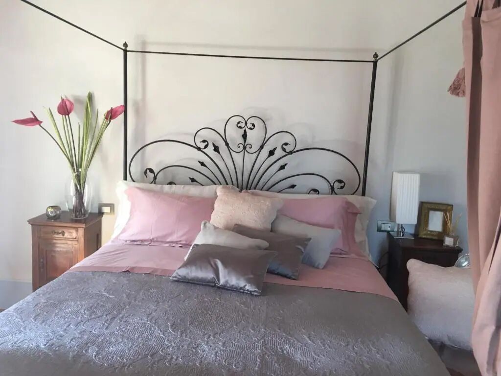 A bed with a metal headboard, multiple pillows, and a vase with flowers on a nightstand.