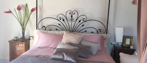 A bed with a metal headboard, multiple pillows, and a vase with flowers on a nightstand.