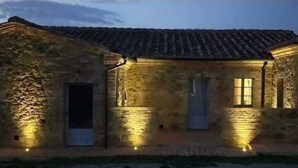A stone building with a tiled roof, illuminated by ground lights. - Cordella in Valdorcia Truffle & Olive Oil Resort - Podere Borgasso (Montalcino)