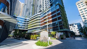 Un bâtiment urbain moderne, doté de plusieurs étages, de grandes fenêtres et d’un espace d’entrée abrité agrémenté de verdure.