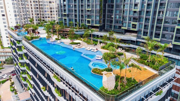 Une piscine sur le toit, dotée de plusieurs niveaux de balcons, entourée de verdure et bordée d’une architecture moderne.