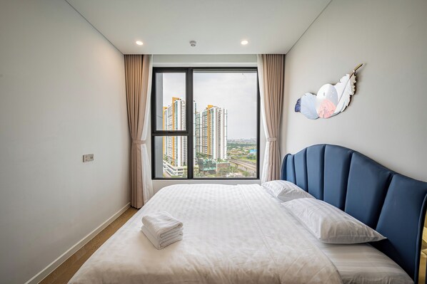 Une chambre d’hôtel avec un grand lit, une vue sur les immeubles qui s’élèvent au loin, visible par la fenêtre, et un élément décoratif mural.