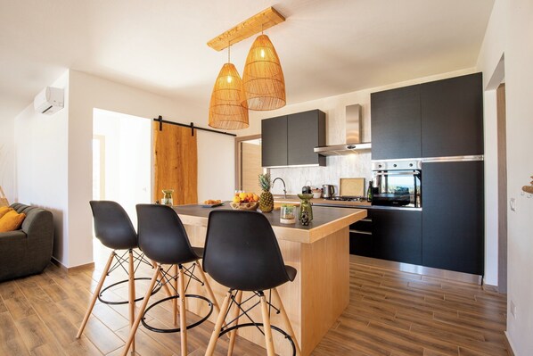 A modern kitchen with a central island, black cabinets, and a stainless steel refrigerator. - Villa MAJU (Marina)