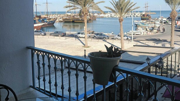 A balcony with a view of a marina, palm trees, and parked cars. - EL MANZEL 102 (HOUMT SOUK)