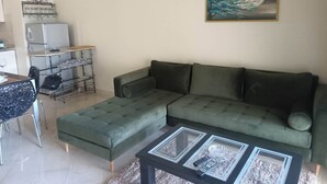 A living room with a green sofa, a glass coffee table, and a dining area with a metal table and chairs. - EL MANZEL 102 (HOUMT SOUK)