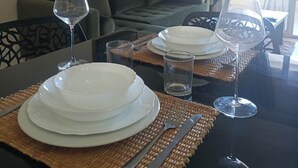 A dining table set with plates, cutlery, and wine glasses, with a view of a living area in the background. - EL MANZEL 102 (HOUMT SOUK)