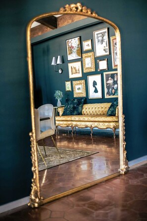 Une pièce dotée d’un grand miroir décoratif qui reflète un mur bleu orné de tableaux encadrés, un canapé doré et un tapis à motifs.