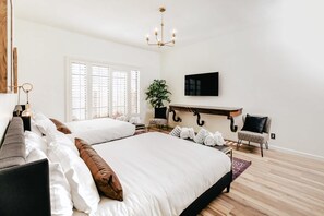 Une chambre avec deux lits, un lustre, une plante en pot, un téléviseur et un plancher en bois.