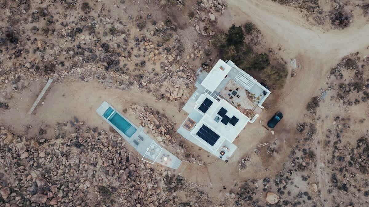 An aerial view of a modern building with a pool, surrounded by rocky terrain.