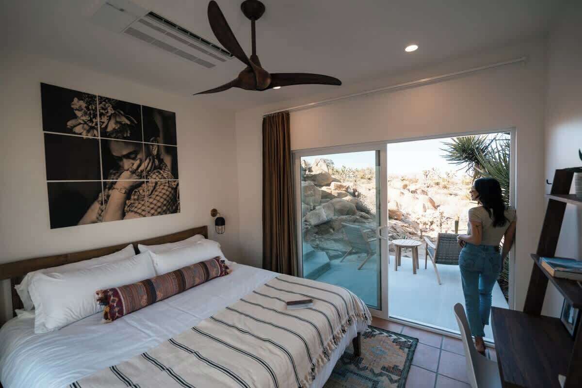 A bedroom with a large bed, a ceiling fan, and a view of a rocky outdoor area through a sliding glass door.