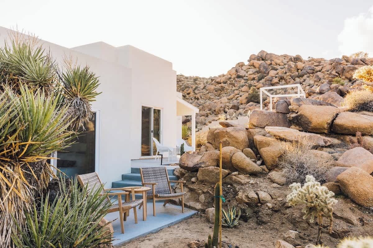 Una casa moderna con un patio, circondata da piante e rocce desertiche.