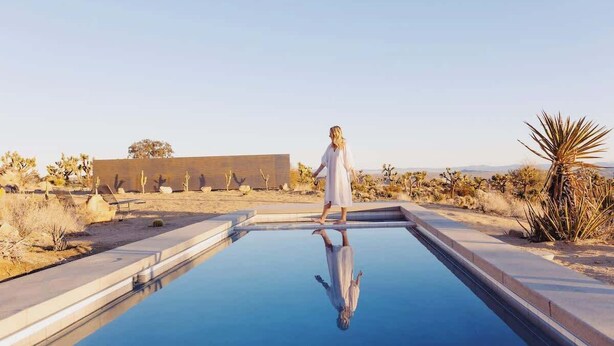 A person standing at the edge of a swimming pool with a desert landscape in the background. - Bolder House • Pool & Spa in Boulders, Views (Joshua Tree)
