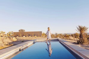 Una persona de pie al borde de una piscina con un paisaje desértico de fondo.