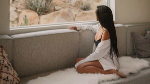 A person sitting on a sofa by a window overlooking a rocky outdoor area with cacti. - Bolder House • Pool & Spa in Boulders, Views (Joshua Tree)