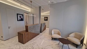 Un área de recepción moderna con piso de mármol, mostrador de madera, dos sillones cómodos y obras de arte enmarcadas en las paredes.