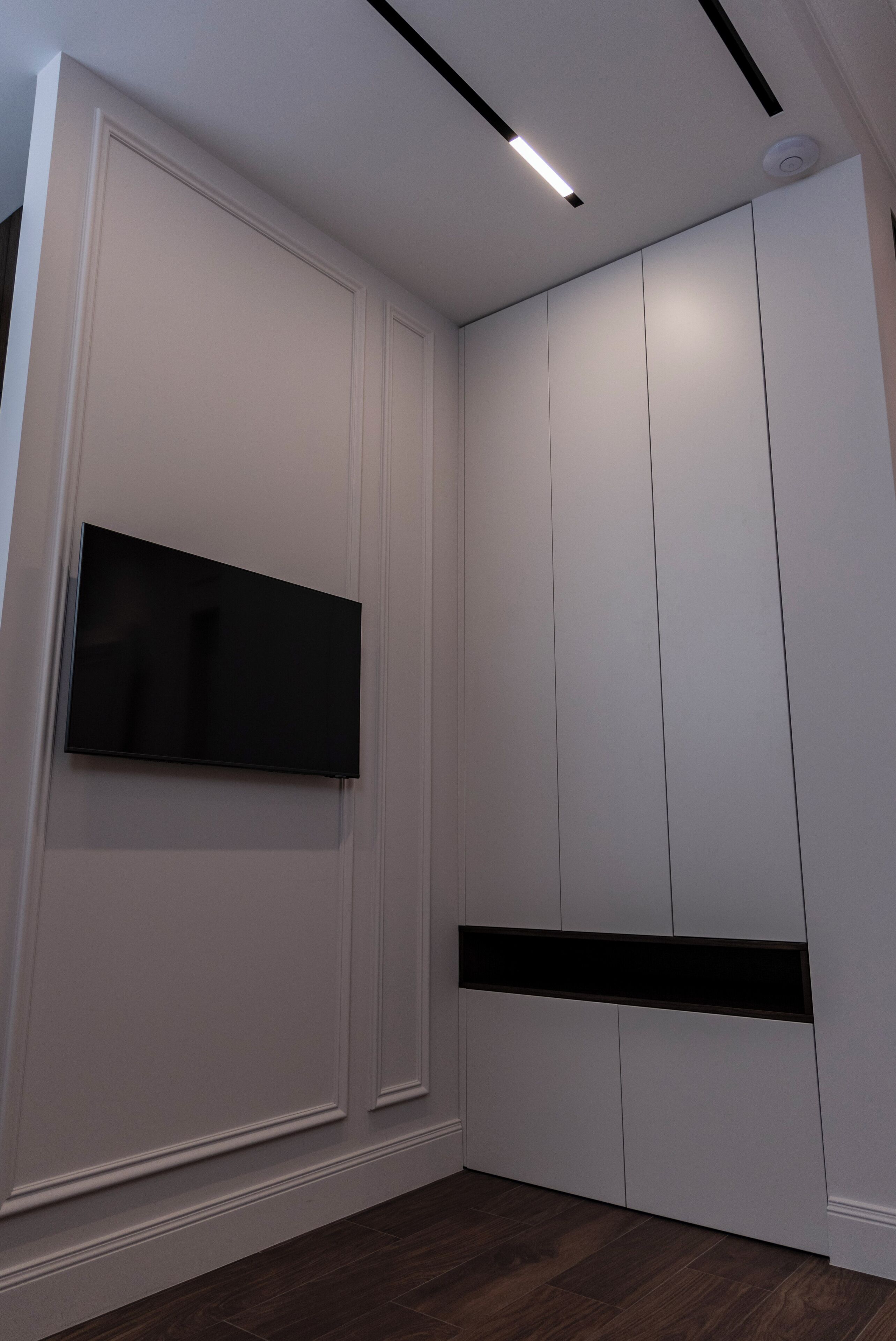 Une pièce moderne avec des armoires blanches intégrées, un téléviseur à écran plat fixé au mur et un plancher en bois foncé.