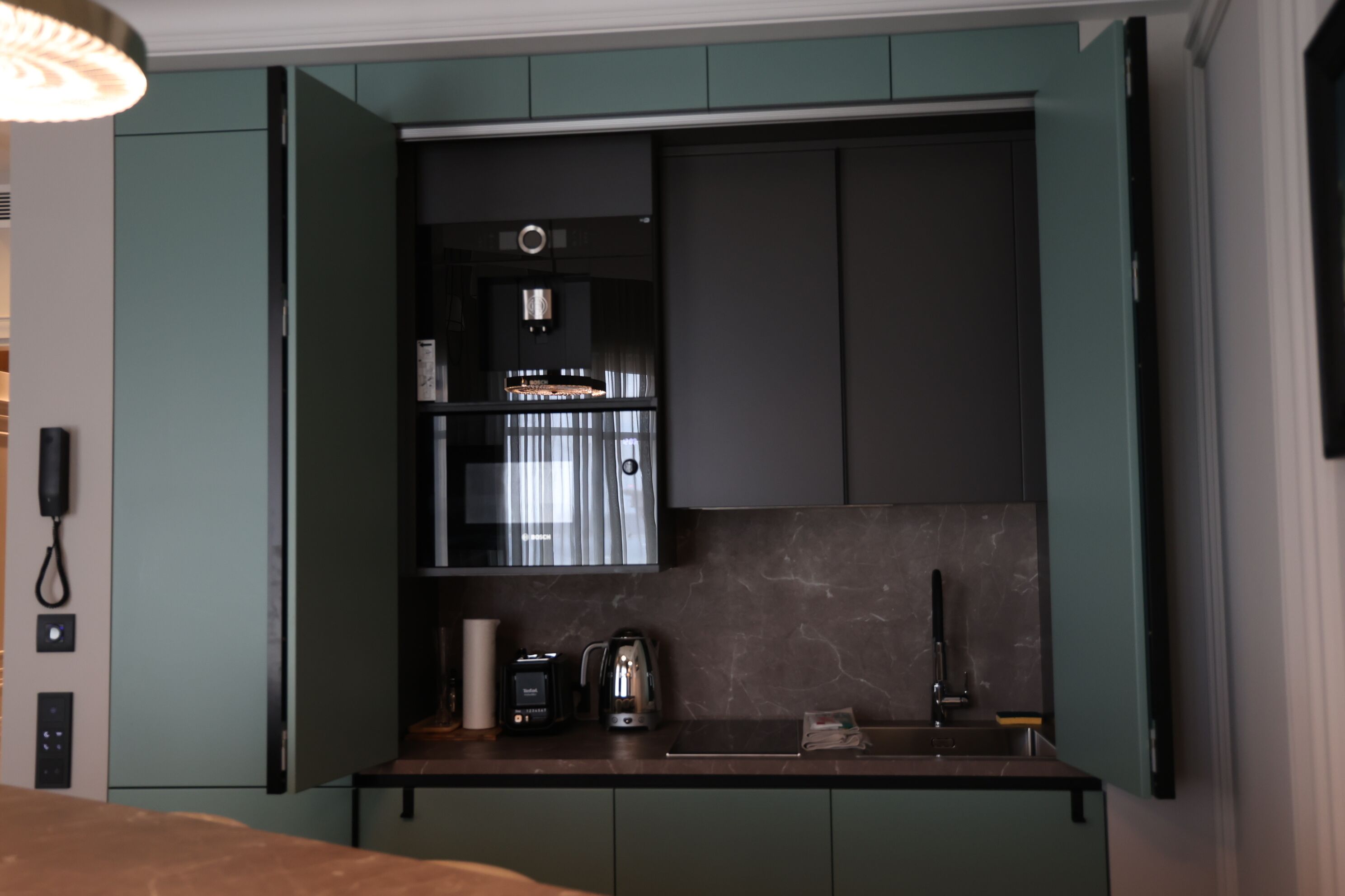 A compact kitchen with dark cabinetry, a coffee maker, and a kettle.