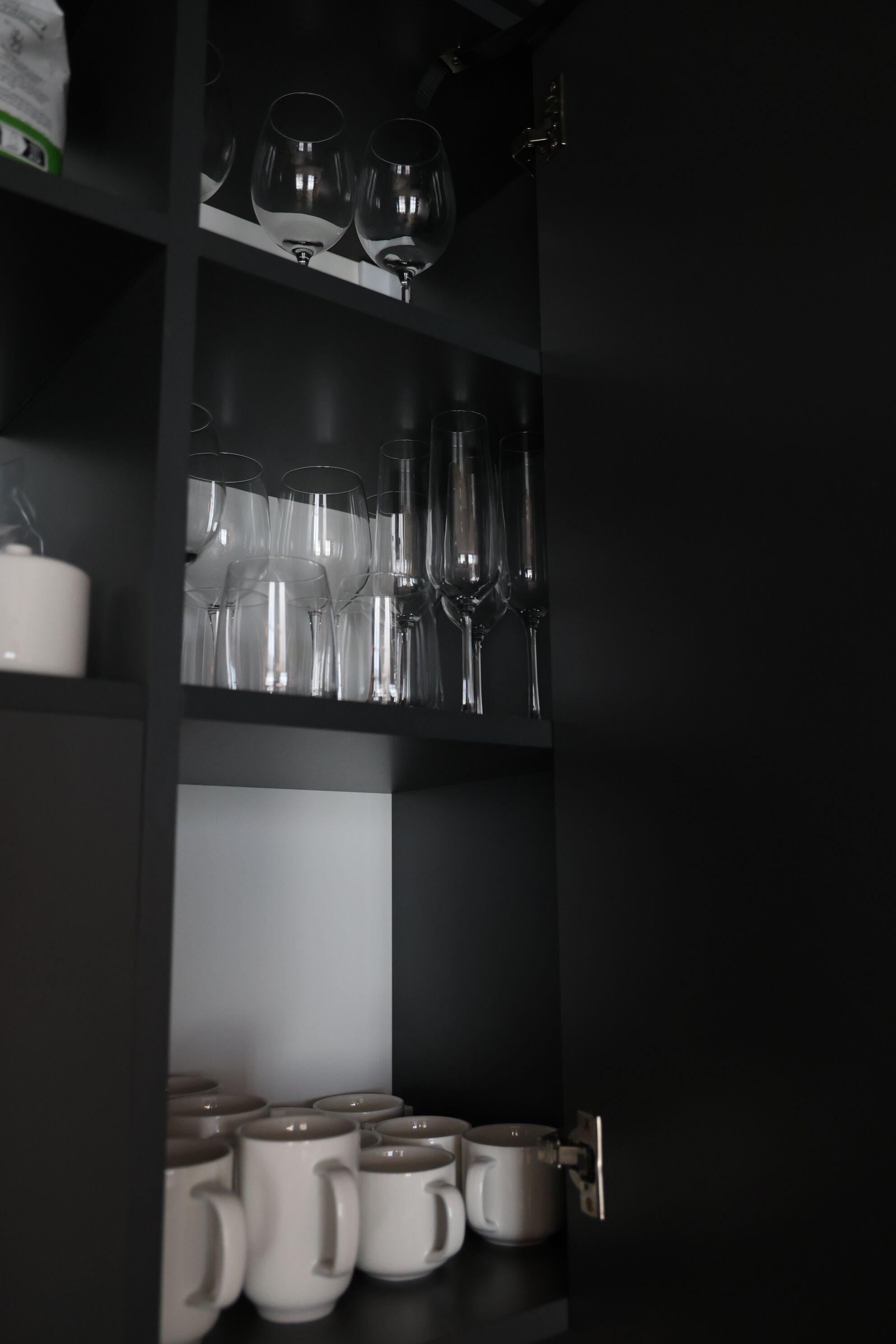 Un mobile nero con ripiani che contengono bicchieri da vino e tazze di ceramica.