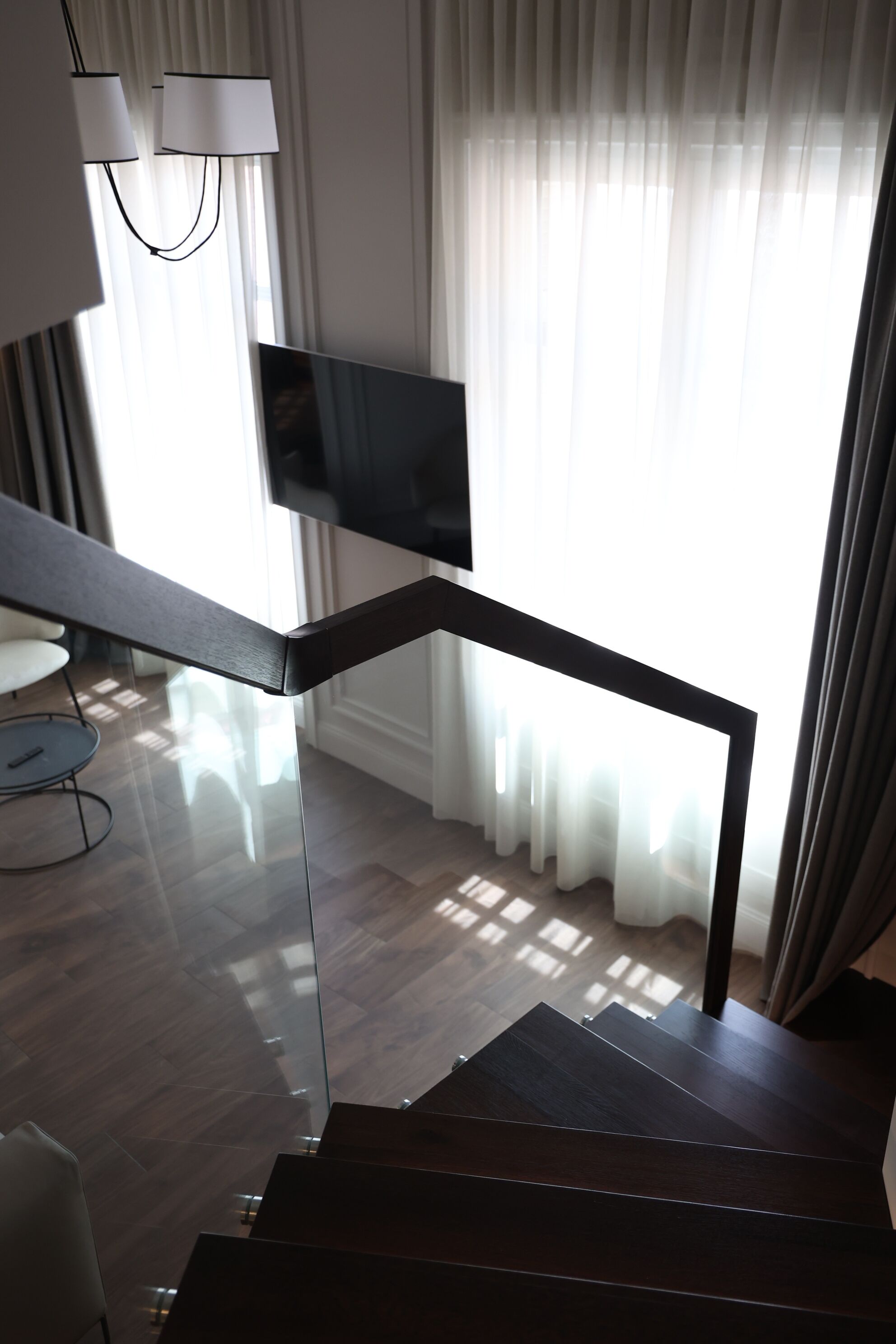 Een moderne trap met een donkere afwerking, die leidt naar een kamer met een wandgemonteerde flatscreen-televisie.