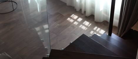 Un escalier moderne à la finition sombre, menant à une pièce où un téléviseur à écran plat est fixé au mur.