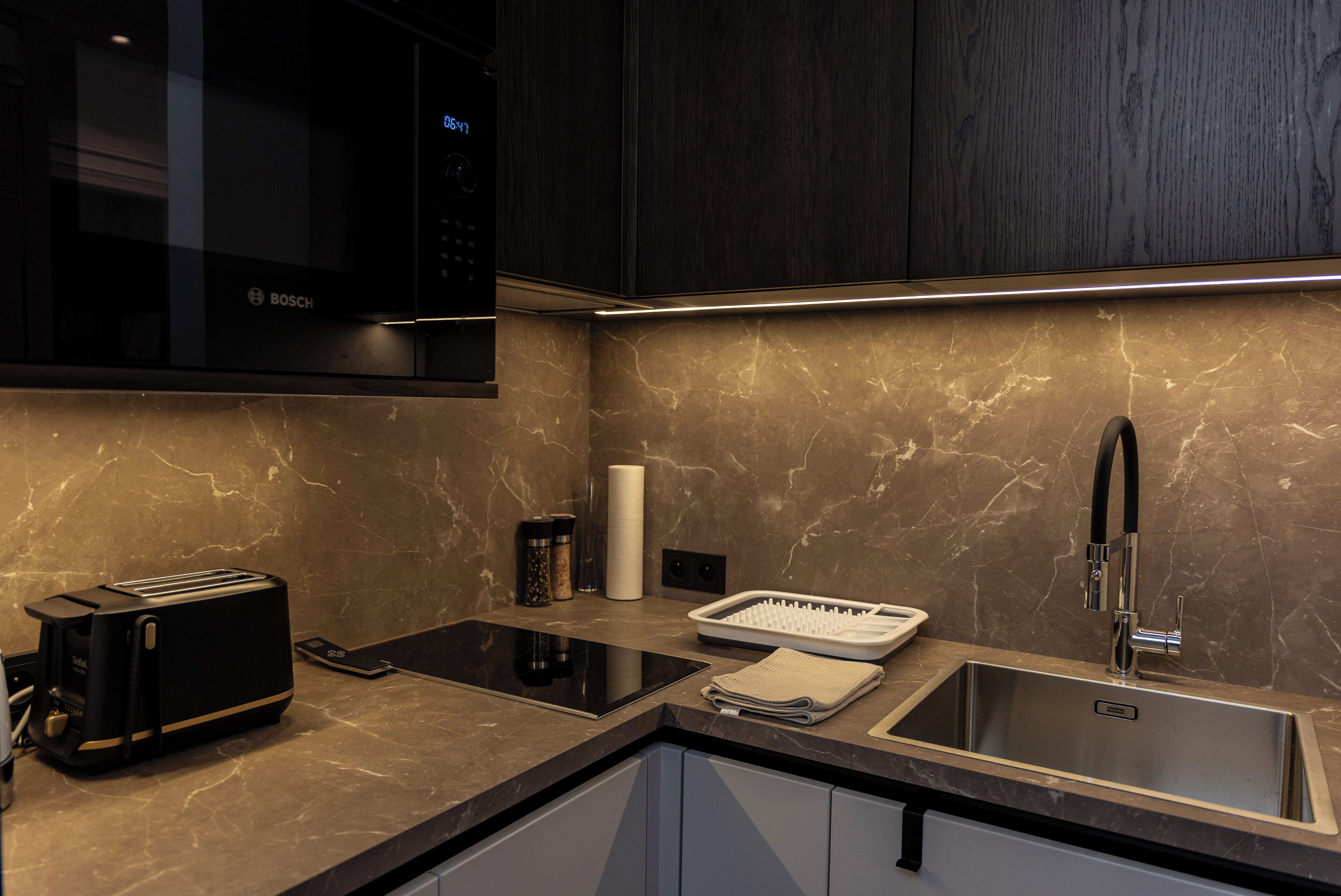 A modern kitchen with a Bosch microwave, a toaster, a sink, and a marble countertop.