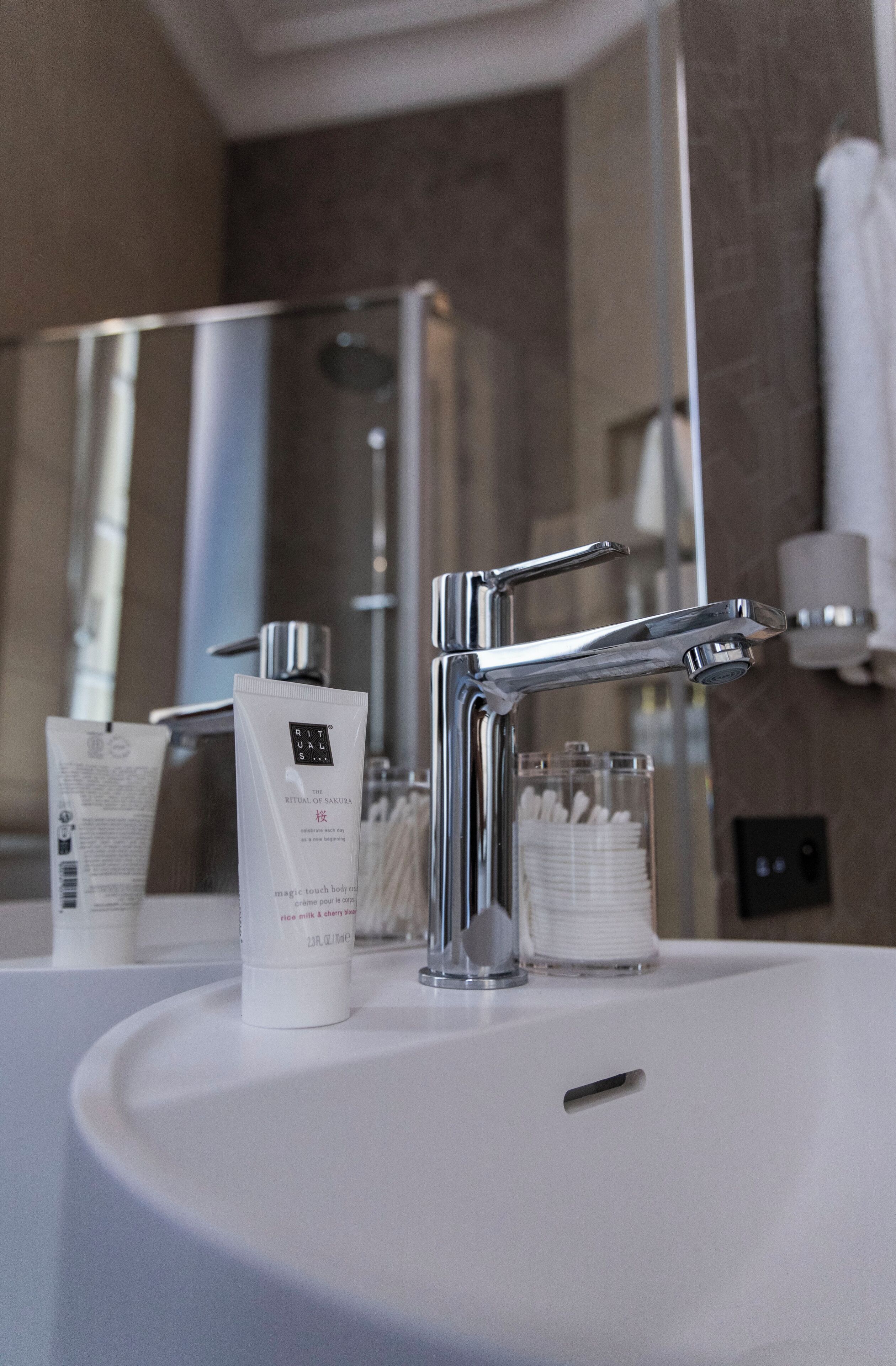 A modern bathroom with a white sink, chrome faucet, and a glass container of cotton swabs.