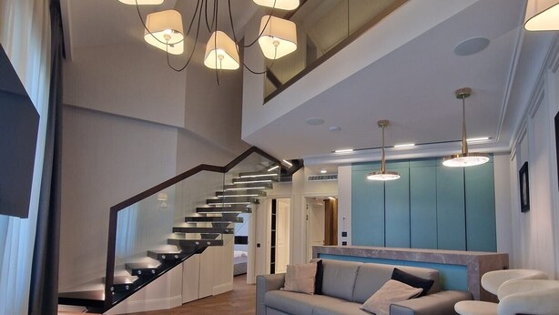 Un interior moderno con una escalera, un sofá e iluminación colgante.
