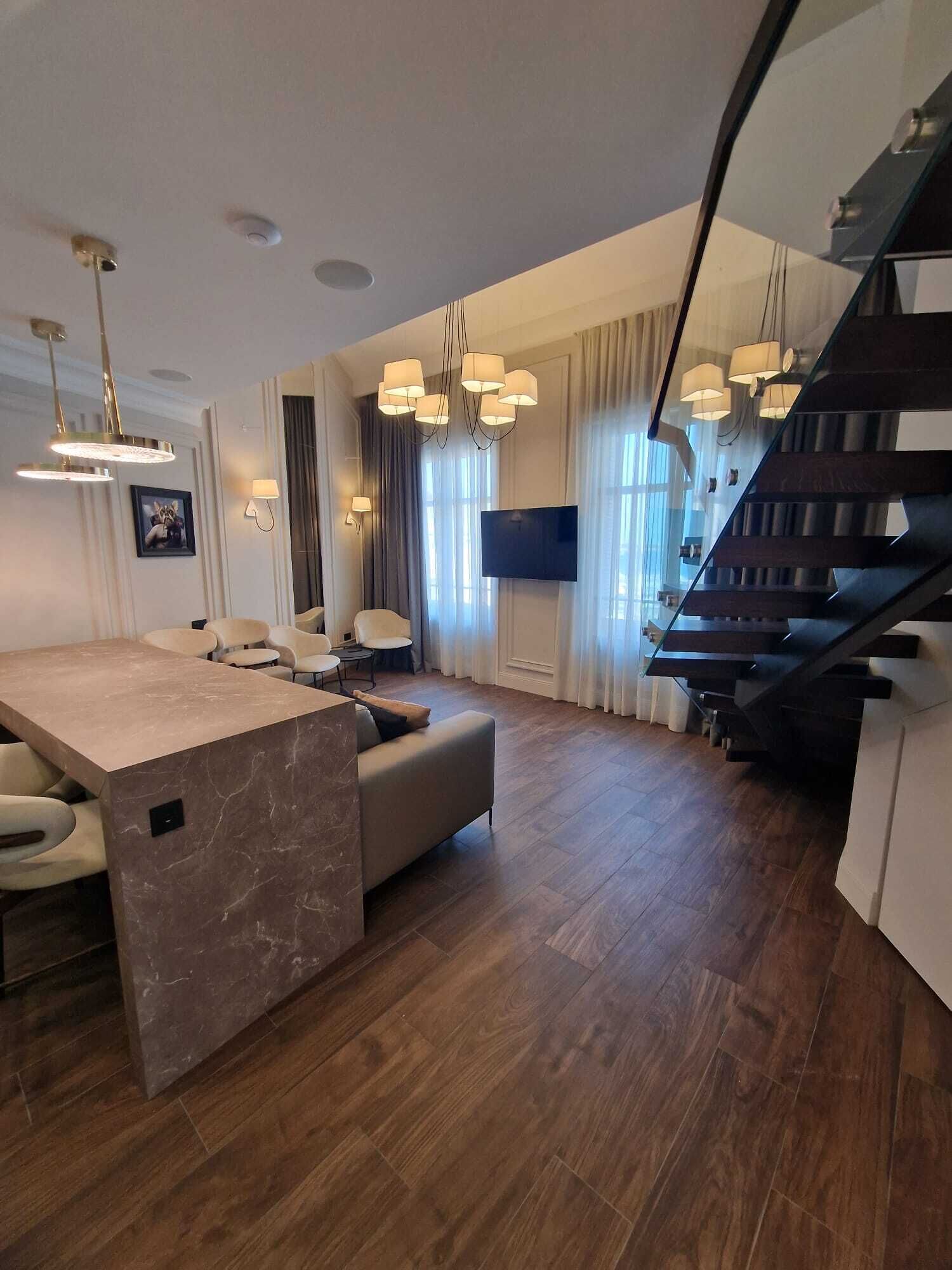 A modern living room with a marble island, a sofa, a dining table, and a staircase.