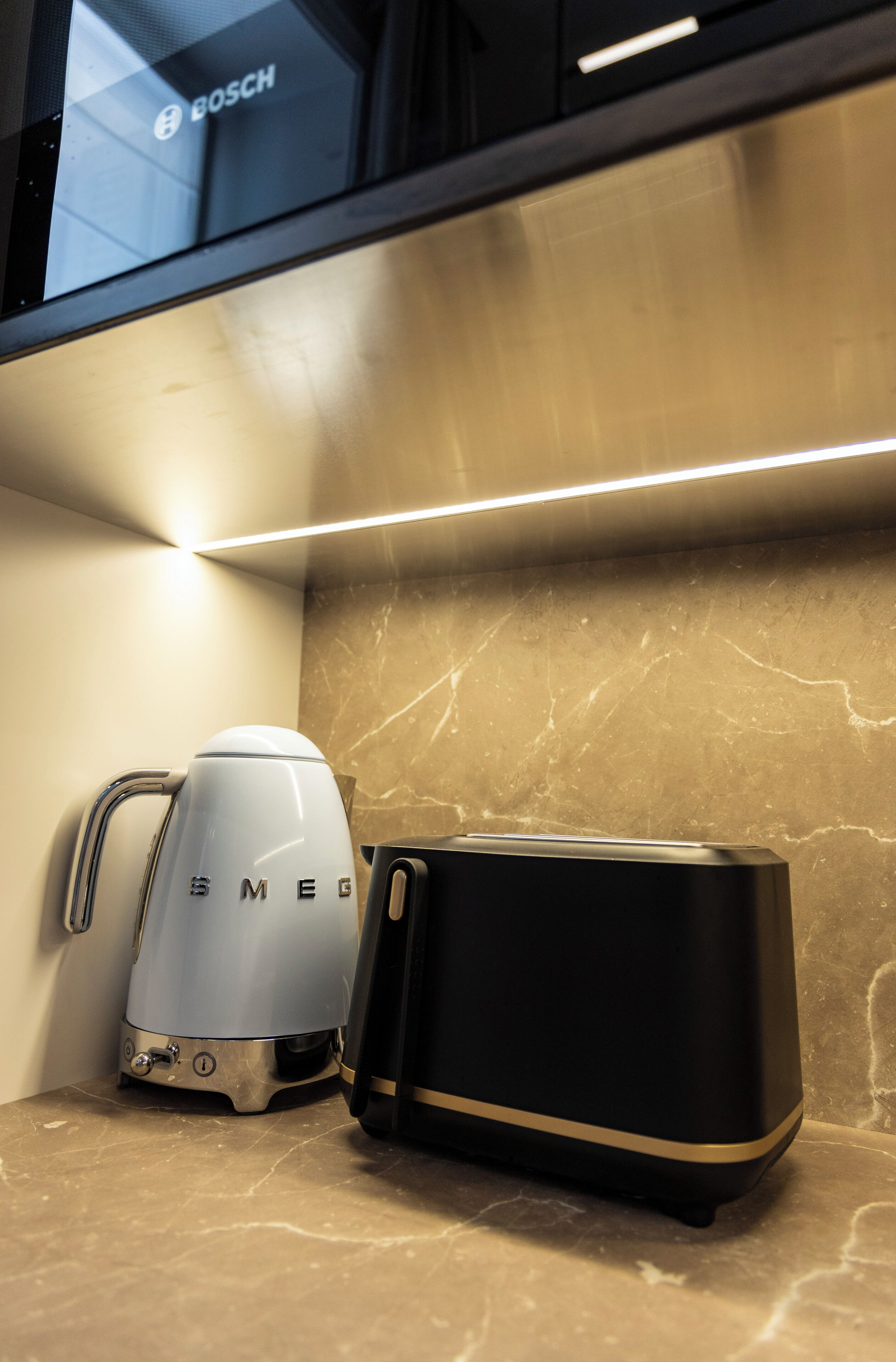 Une cuisine équipée d’une machine à café Bosch et d’un appareil noir, qui pourrait être un grille-pain ou un cuiseur à riz, posé sur un plan de travail en marbre.