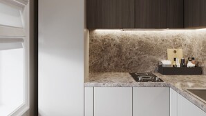 Una cocina moderna con estufa integrada, armarios blancos, alacenas superiores de madera oscura y encimera de mármol.
