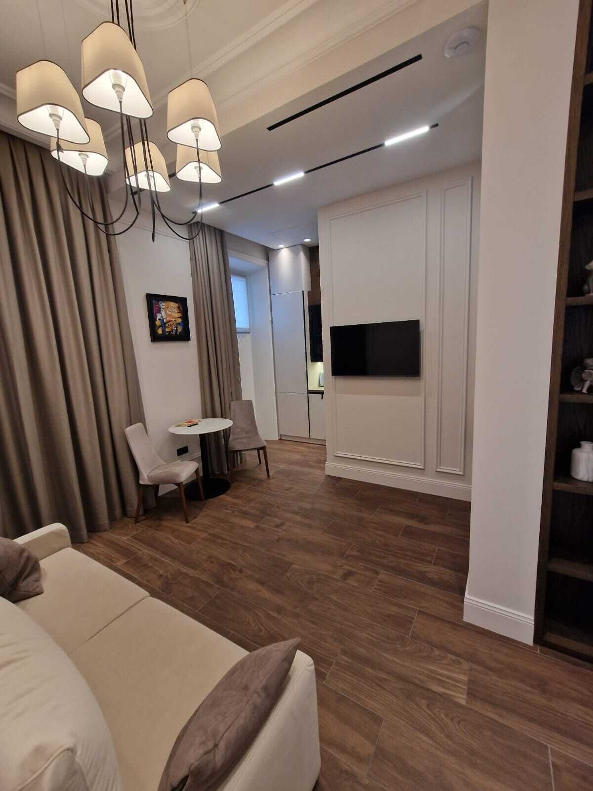 Un salon moderne comprenant un canapé, une table à manger avec des chaises, un téléviseur fixé au mur et une bibliothèque.