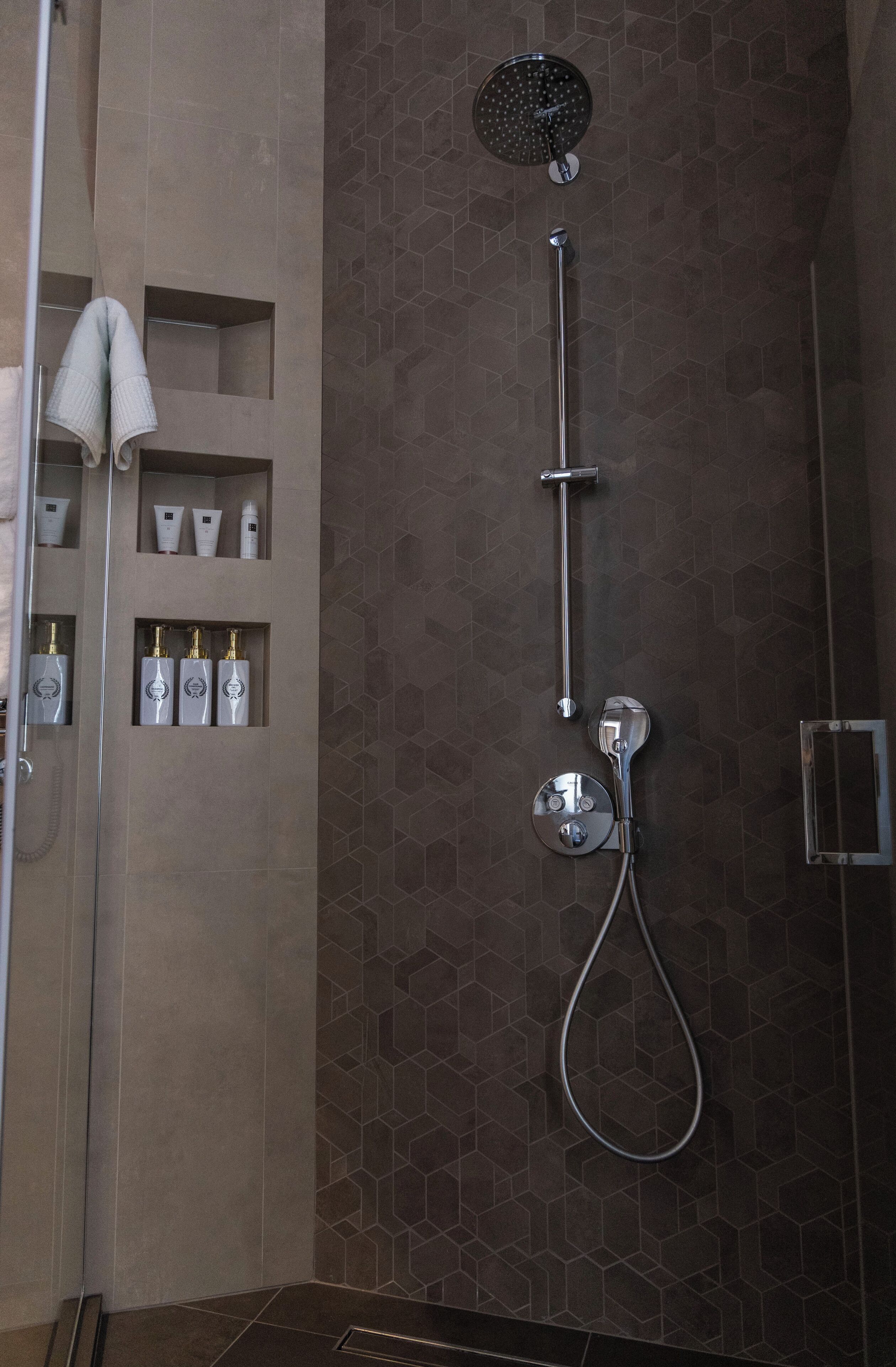 A modern shower area with a rain showerhead, handheld shower, and a handheld showerhead with a curved design.