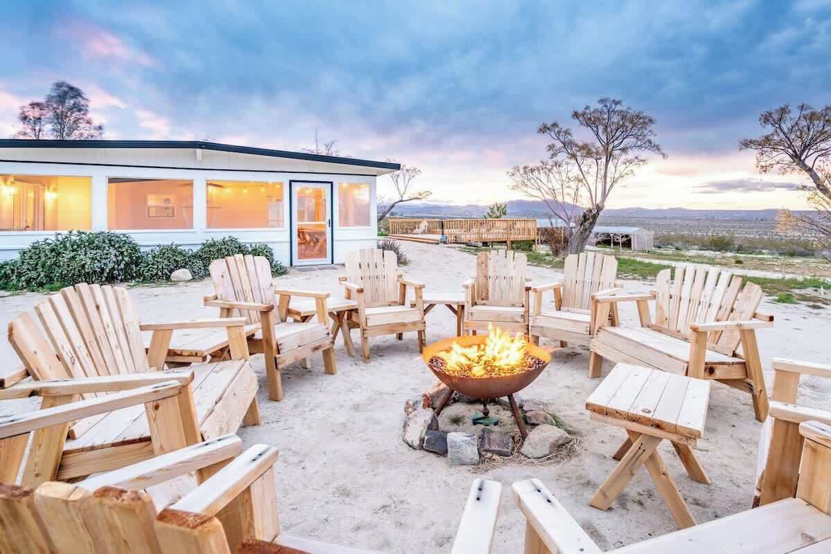 A beachside outdoor seating area with wooden Adirondack chairs and a central fire pit.