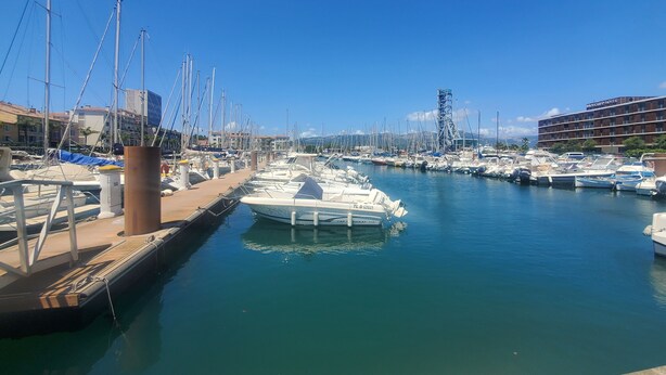 Un port de plaisance avec des bateaux amarrés, un hôtel appelé Mercure en arrière-plan et un ciel bleu dégagé.