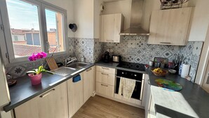 Une cuisine moderne avec des meubles en bois, un plan de travail noir et une fenêtre donnant sur des immeubles.
