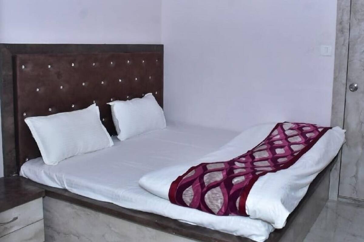 Un lit simple avec une tête de lit en bois, du linge de lit blanc et un plaid à motifs.