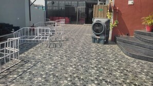An outdoor terrace with a tiled floor, metal railings, a fan, and a staircase leading to a building entrance. - Hotel Wonder View By GRB Stays (Kota)