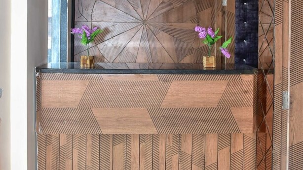 A reception desk with a geometric wood panel design and two purple flowers in vases. - Hotel Wonder View By GRB Stays (Kota)