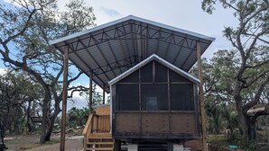 Una cabaña de madera con techo metálico y un amplio ventanal, rodeada de árboles.