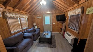 Un interior de cabaña acogedor con techo de madera, un sofá, una mesita de centro, un televisor y un cartel que dice "Welcome".