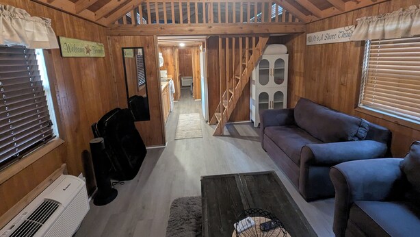 Interior de una cabaña de madera con sala de estar, una escalera y una cocina.