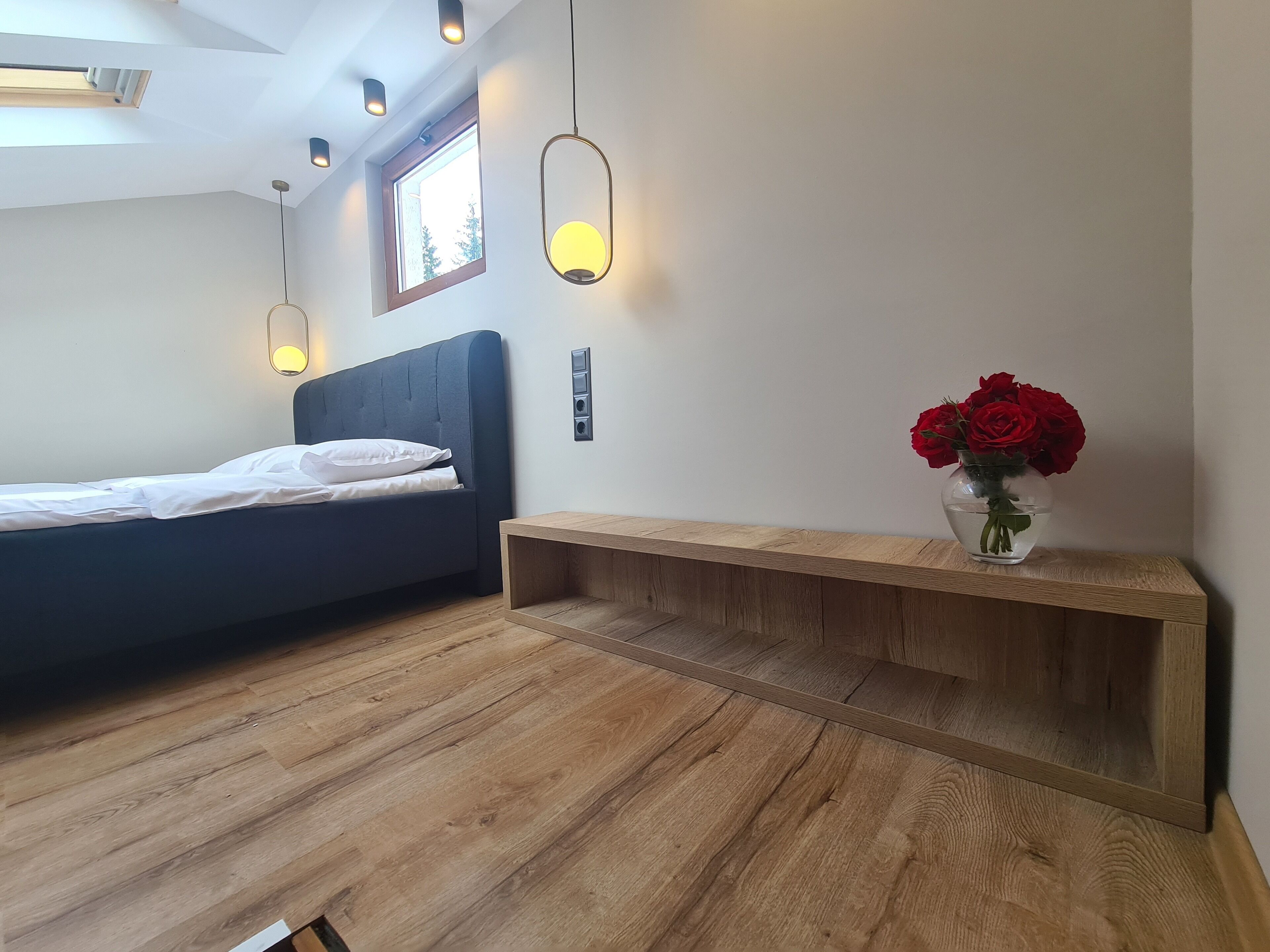 A bedroom with a bed, bedside table, and a vase with red roses.