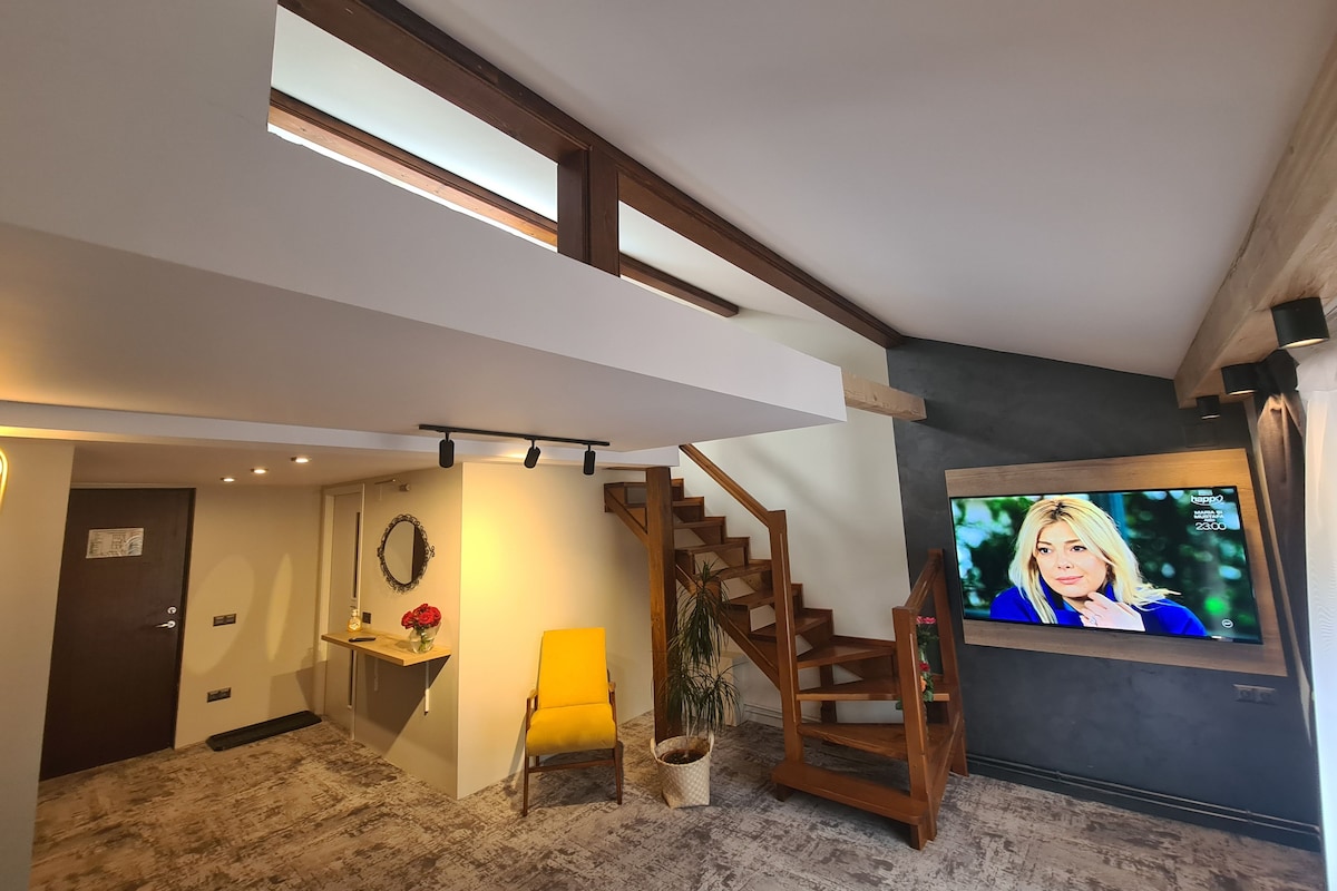 Una sala de estar moderna con una escalera de madera, un televisor montado en la pared y una mesita con un jarrón de flores.