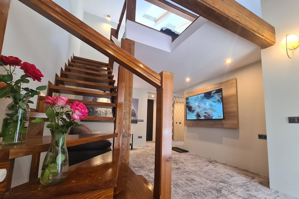 A wooden staircase with a glass enclosure leading to a high ceiling with a skylight.