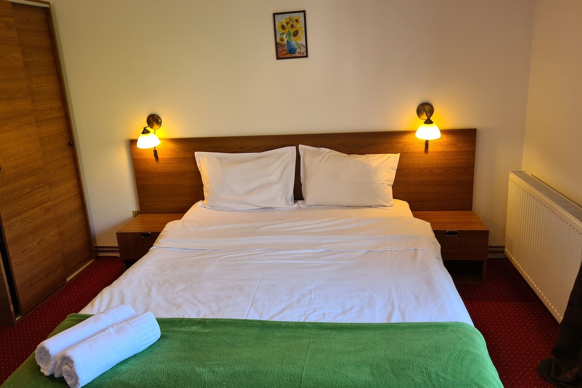 Una cama bien hecha con sábanas blancas, dos almohadas y una toalla verde sobre un suelo cubierto de alfombra roja.