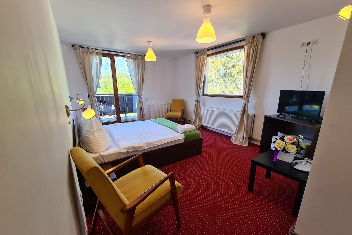 A hotel room with a bed, a desk, a chair, a TV, and a window with curtains.
