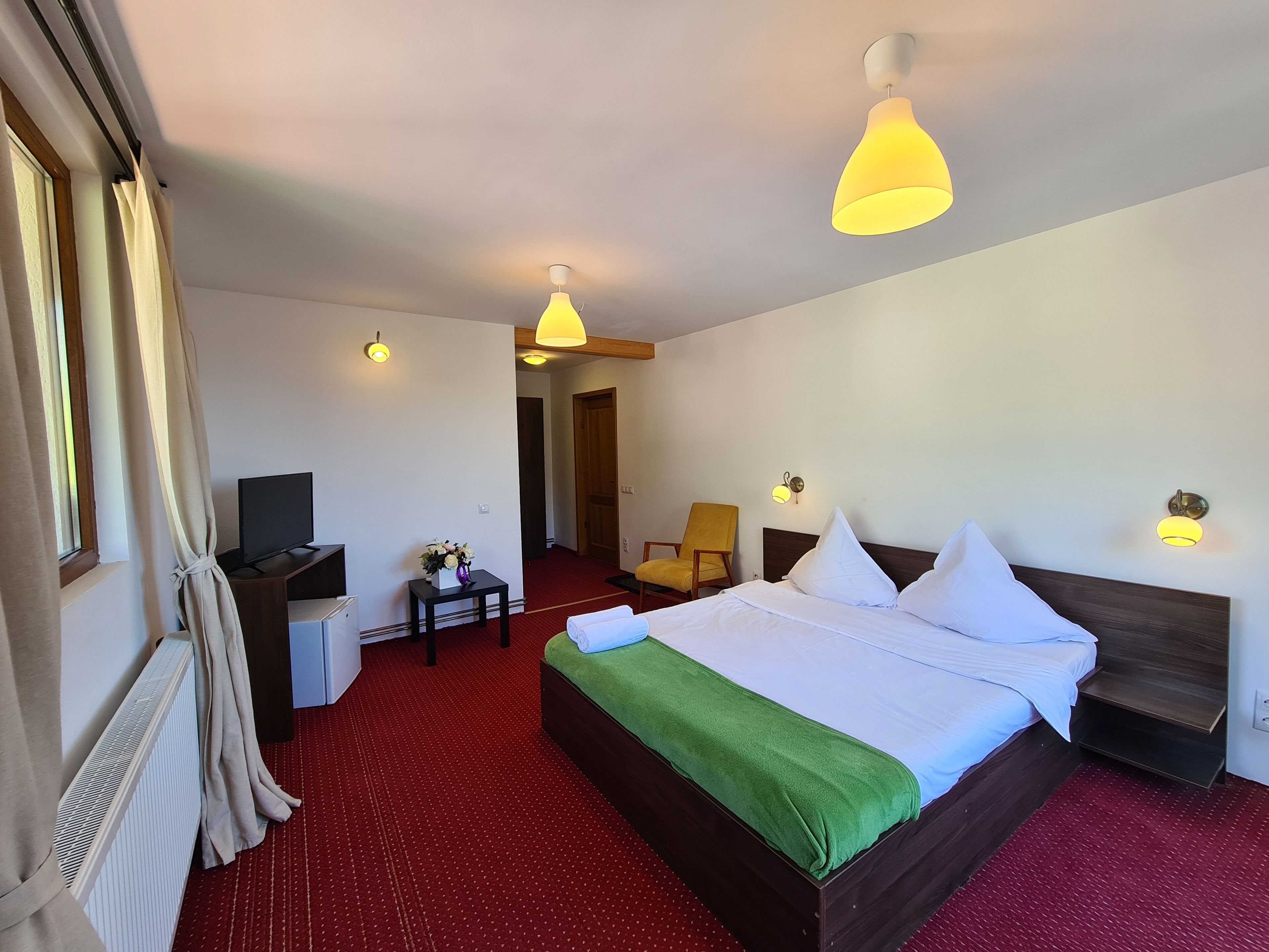 Habitación de hotel con una cama grande, un escritorio con computadora, una silla y una alfombra roja.